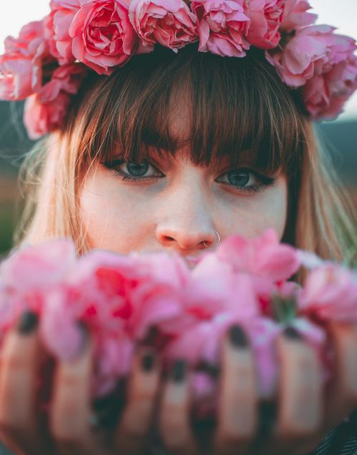 Free Close-up portrait of a woman wearing a pink flower crown, holding flowers in her hands and looking at the camera. Stock Photo