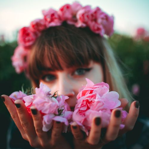 Free A woman with a floral crown gently holds pink flowers, creating a soft, dreamy aesthetic. Stock Photo