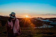 一名戴着围巾和帽子的妇女在黄金时段的美丽田野上观看日出