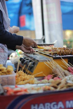 A street vendor grilling skewers at an outdoor food market during the day.