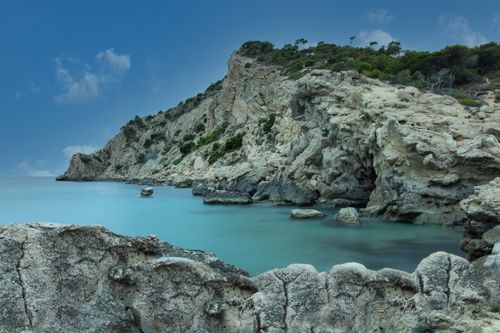 Free Tranquil rocky coastline at dusk with calm waters and lush greenery. Stock Photo