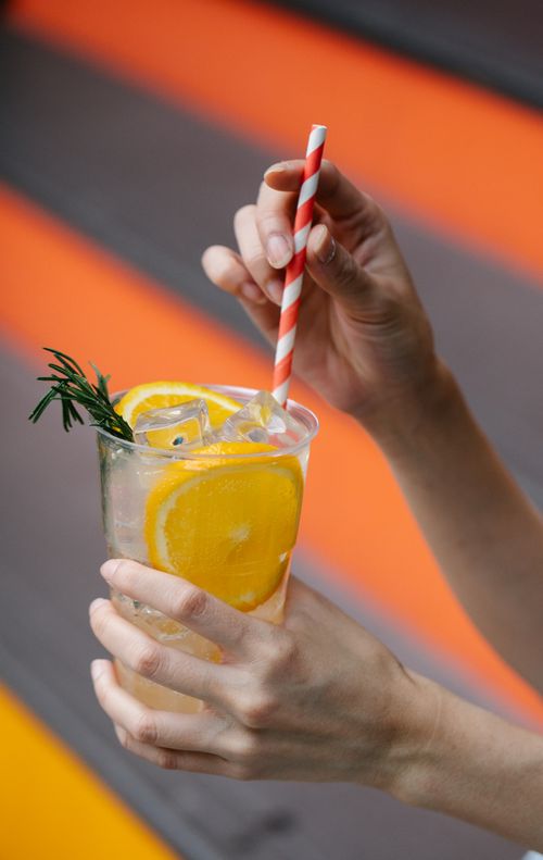 Free Close-up of hands holding an iced citrus beverage with orange slices and rosemary garnish. Stock Photo