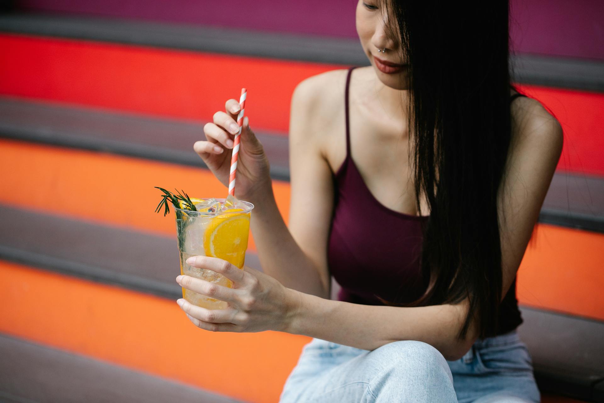 Young woman sipping lemonade with orange slices outdoors. Refreshing and lively.