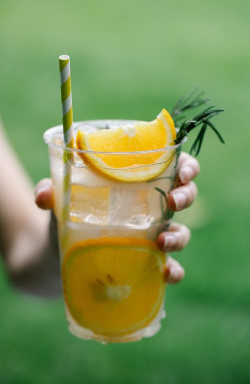 Person Holding A Lemonade With Orange Slices In Plastic Cup