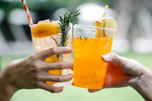 Free Close-up of hands toasting with citrus-infused drinks in outdoor setting. Stock Photo