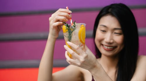 Photo of a Woman Smiling while Holding a Cup with Orange Juice