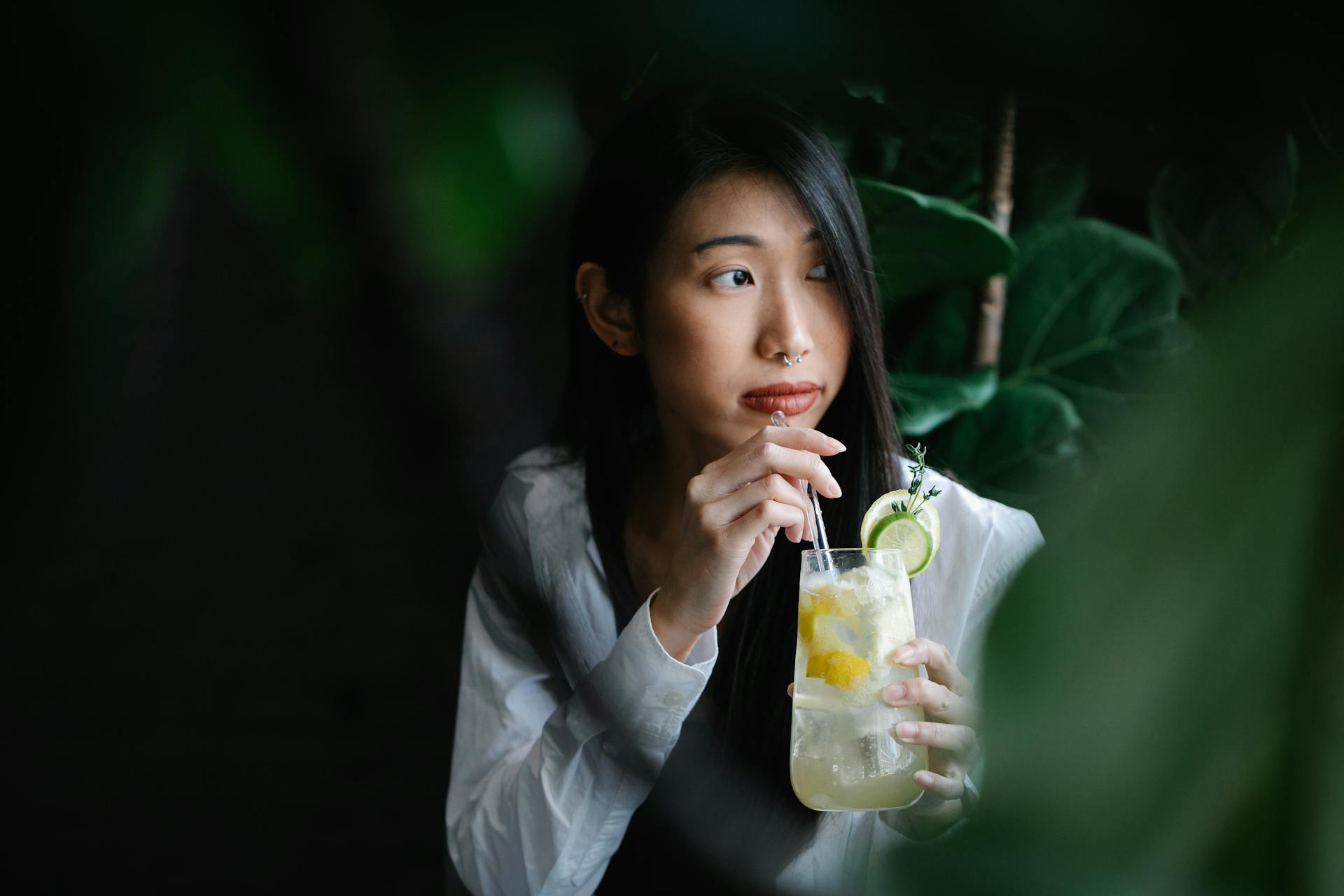 Portrait of a woman sipping lemonade through straw in a serene setting.