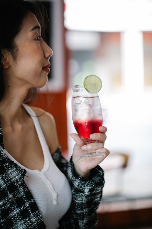 Free Asian woman holding a refreshing iced drink with a lime slice indoors. Stock Photo