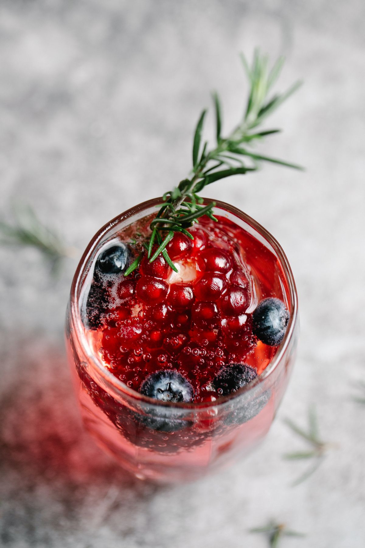 Glass of red berry spritzer with blueberries and a sprig of rosemary