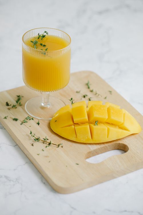 Free Delicious mango juice with fresh mango slices on a wooden board, garnished with herbs. Stock Photo