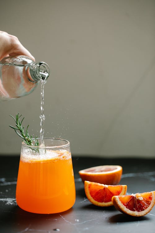 Person Pouring Alcohol On Fresh Fruit Juice Drink