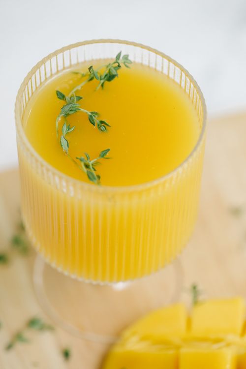 Free Close-up of vibrant mango juice garnished with fresh herbs in a glass. Stock Photo