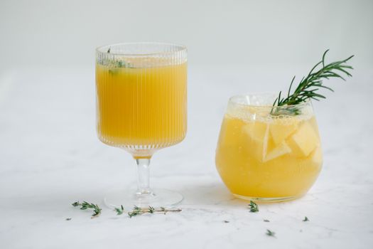 Two glasses of citrus juice garnished with fresh herbs on a marble surface.