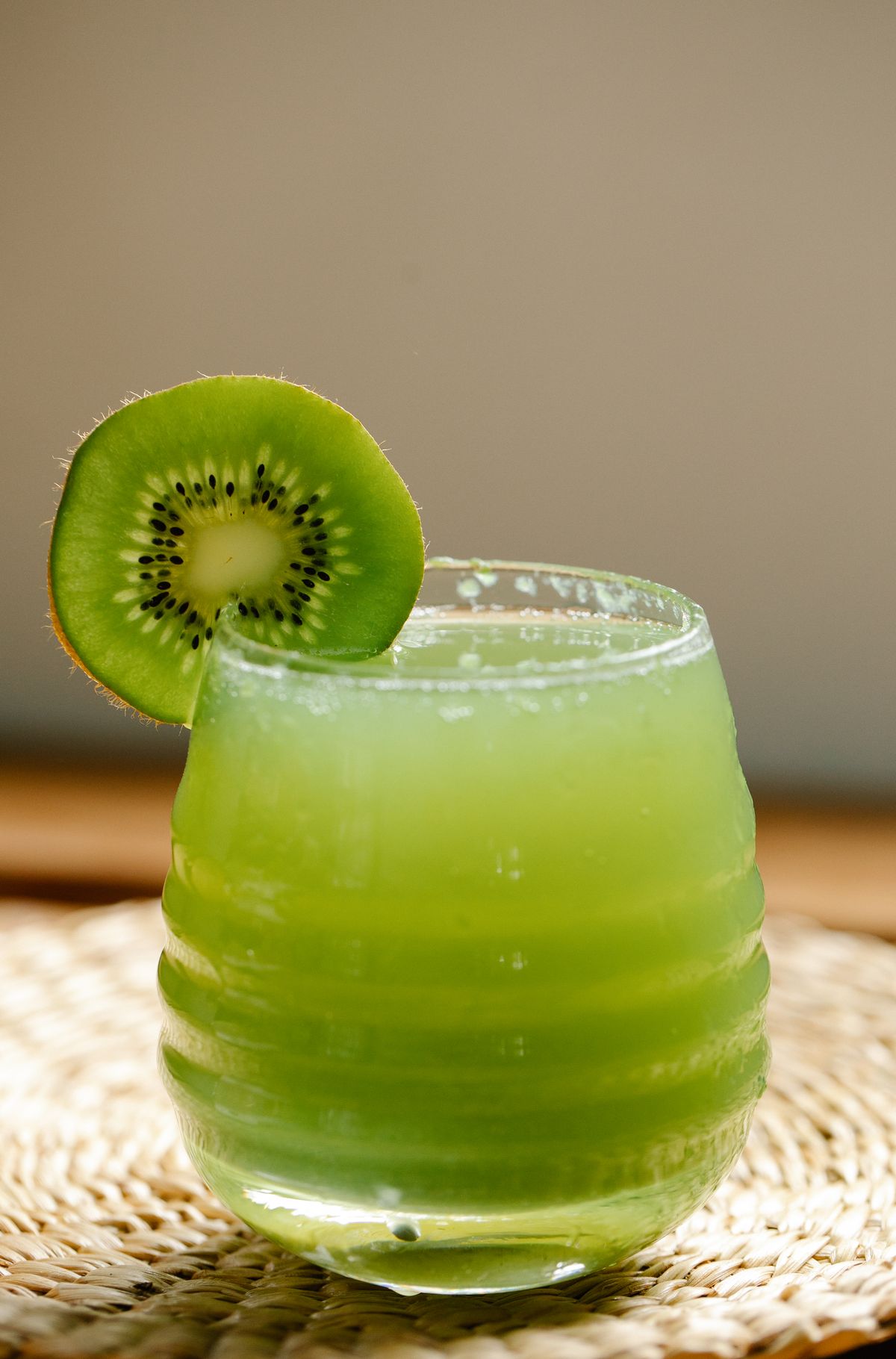 Vivid green kiwi drink in a ribbed glass with a kiwi slice on the rim
