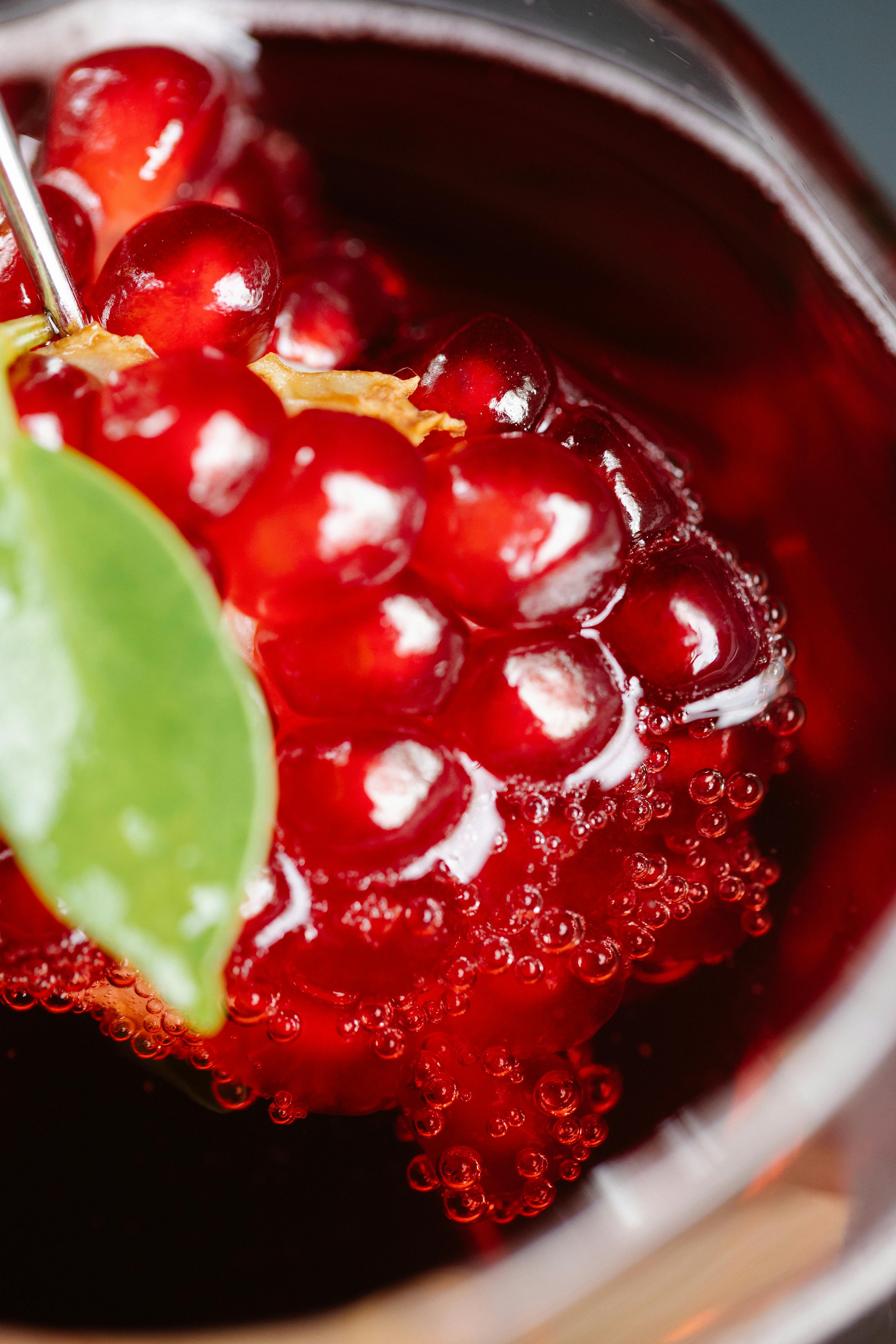 Macro photography of vibrant red pomegranate seeds with green leaf detail.