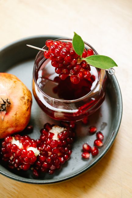 Glass of deep red pomegranate juice with fresh pomegranates on plate