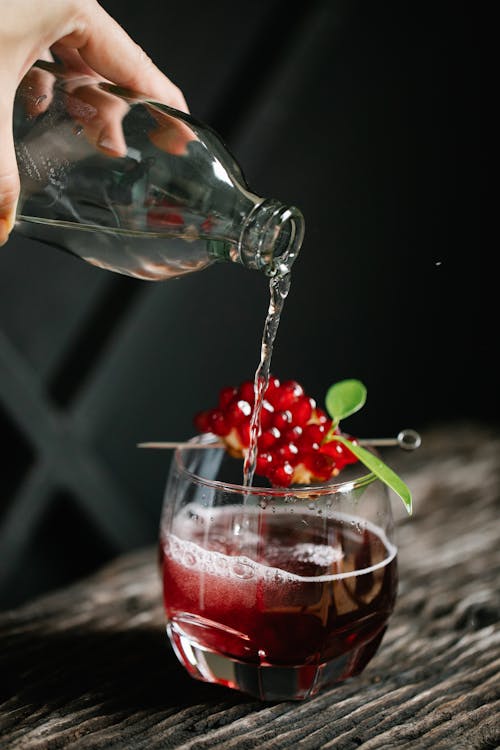 Free A Person Pouring a Water on a Drinking Glass with Pomegranates Stock Photo