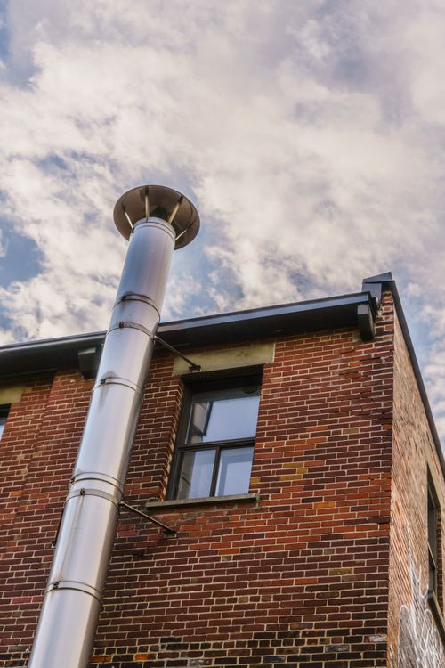 Free Close-up of a modern brick building featuring a tall steel pipe against a cloudy sky. Stock Photo