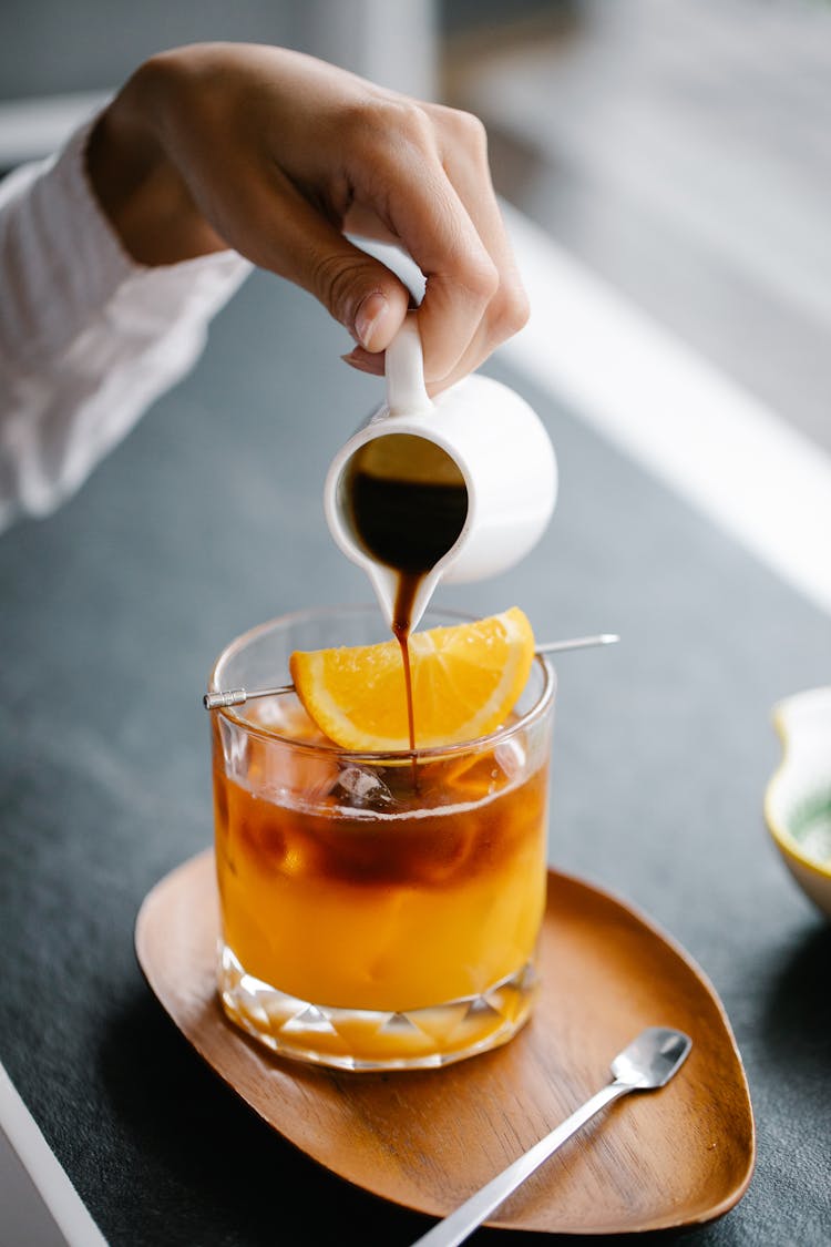 Woman Pouring Espresso Into Orange Juice 