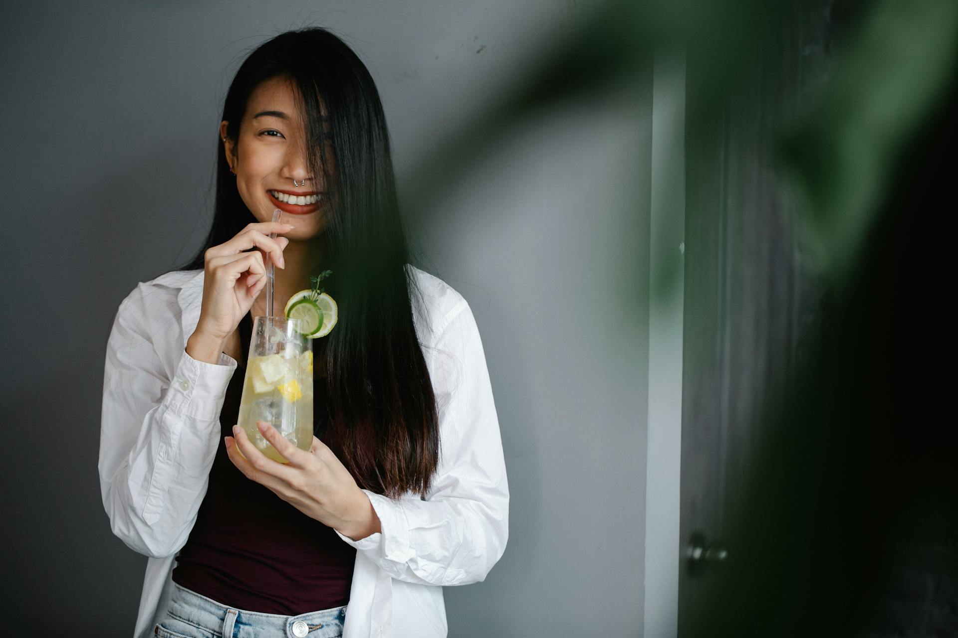 Young woman with long hair enjoying a refreshing lemonade drink indoors while smiling.