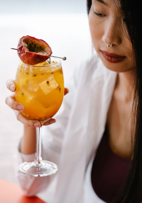 Free Close-up of a woman with septum piercing holding a vibrant passionfruit cocktail in a glass. Stock Photo
