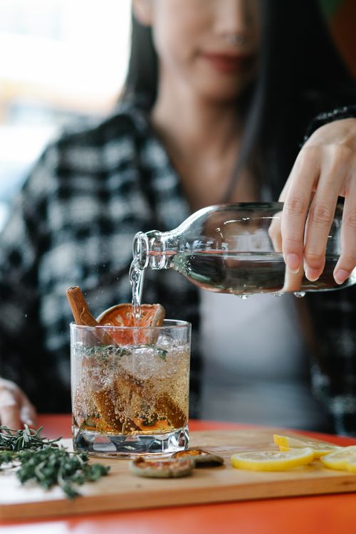 Free A woman pours water into a cocktail glass filled with citrus slices and herbs. Stock Photo