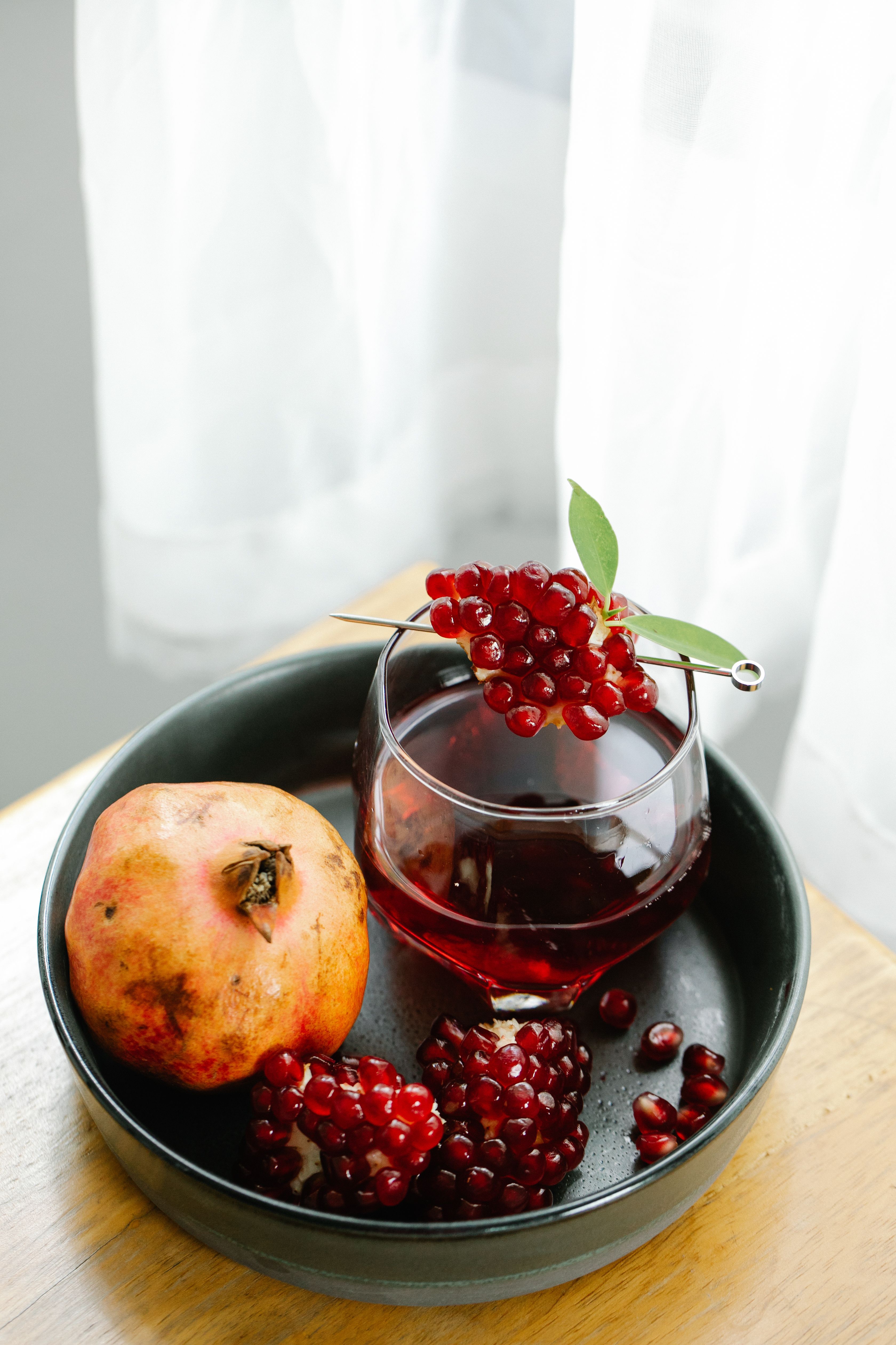Pomegranate juice elegantly served in a glass with fresh berries on a tray.