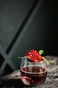 A sophisticated cocktail garnished with pomegranate seeds and a leaf on a rustic tabletop.