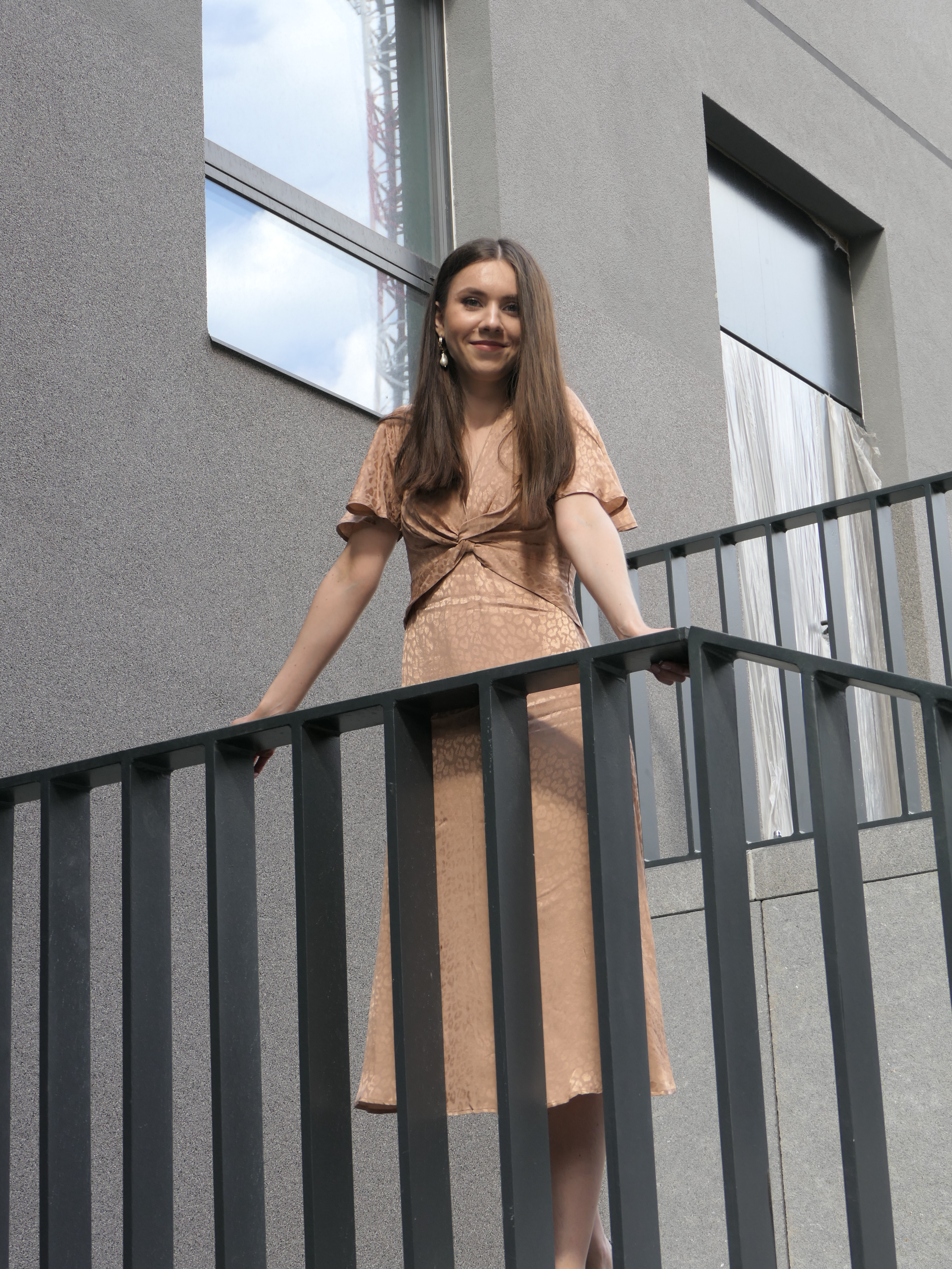 Fashionable woman in stylish dress posing on a modern building's balcony.
