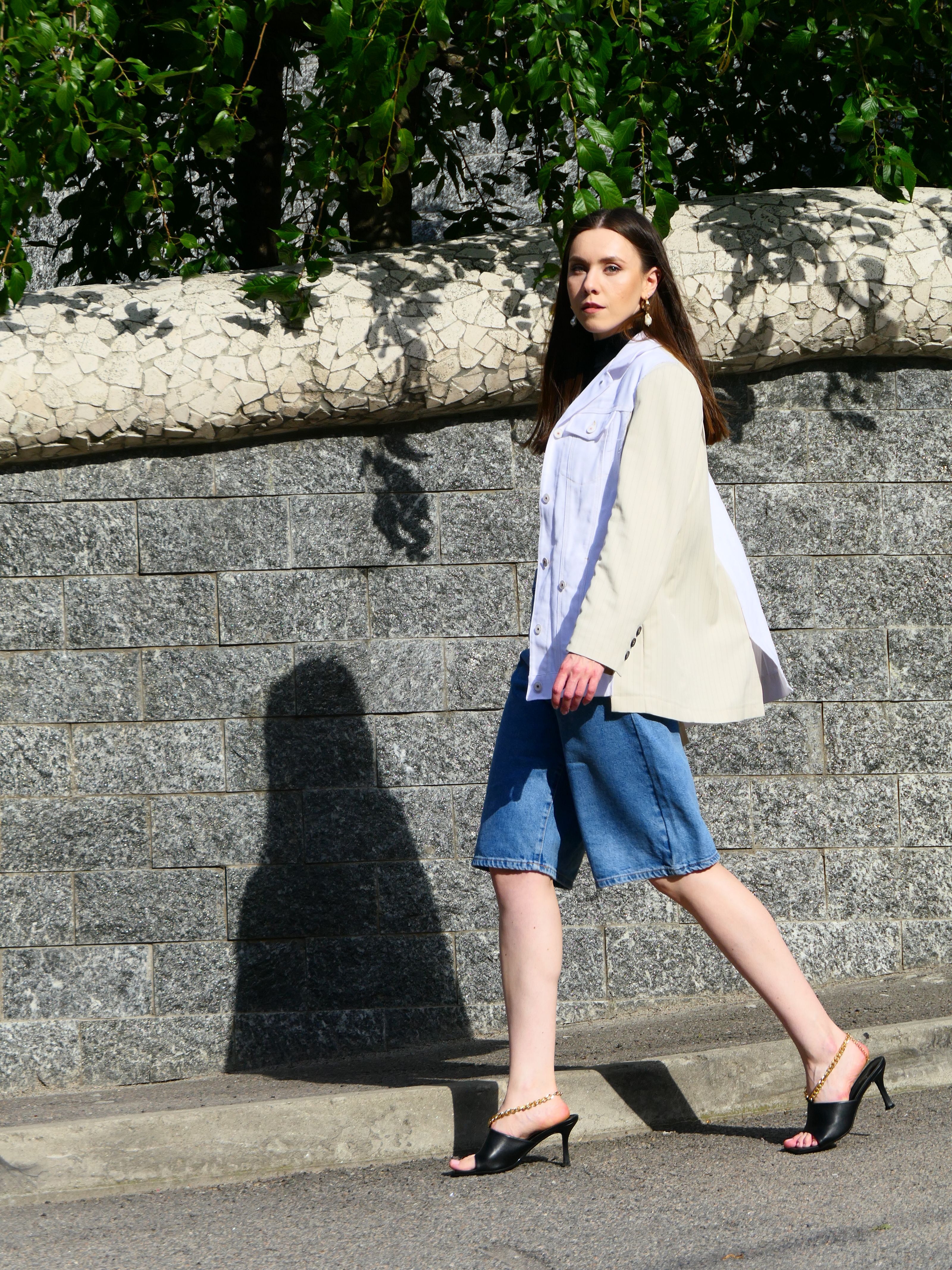 Mulher estilosa em denim e blazer caminhando com confiança ao ar livre.