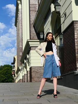 Confident woman posing outdoors in urban setting wearing stylish denim and jacket.