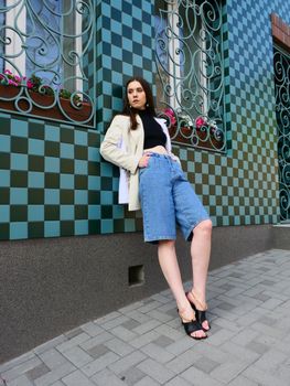 Stylish woman leans against a decorative geometric wall in an urban setting, showcasing modern fashion.