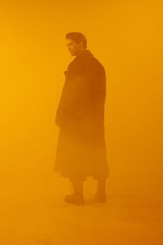 A person in a dark coat stands against a vivid orange background in a conceptual cyberpunk style.