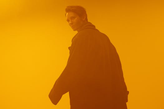 A person in a black coat standing in an orange-hued studio, evoking a dystopian cyberpunk feel.