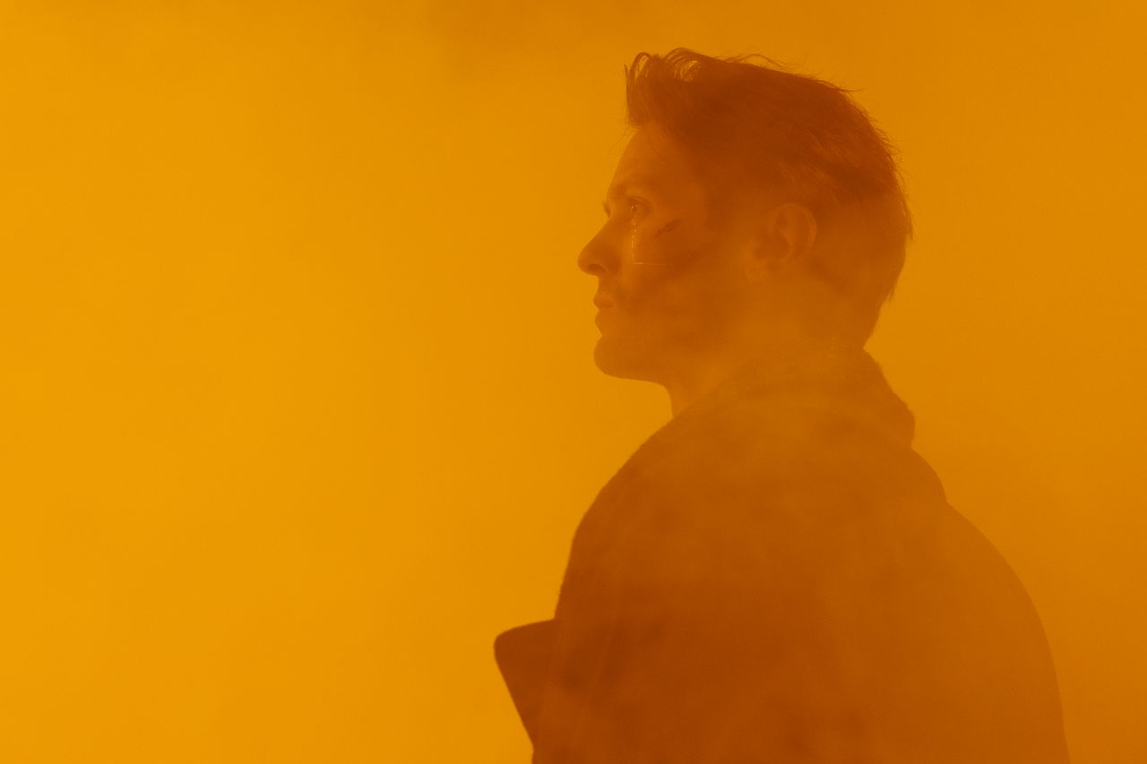 a conceptual close up portrait of a man in a dystopian orange hued set