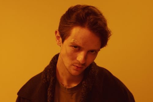 Free Close-up of a man with a cyberpunk aesthetic against a warm orange background. Stock Photo