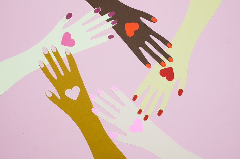 Artistic paper cutout hands with hearts symbolize unity and love on a pink background.