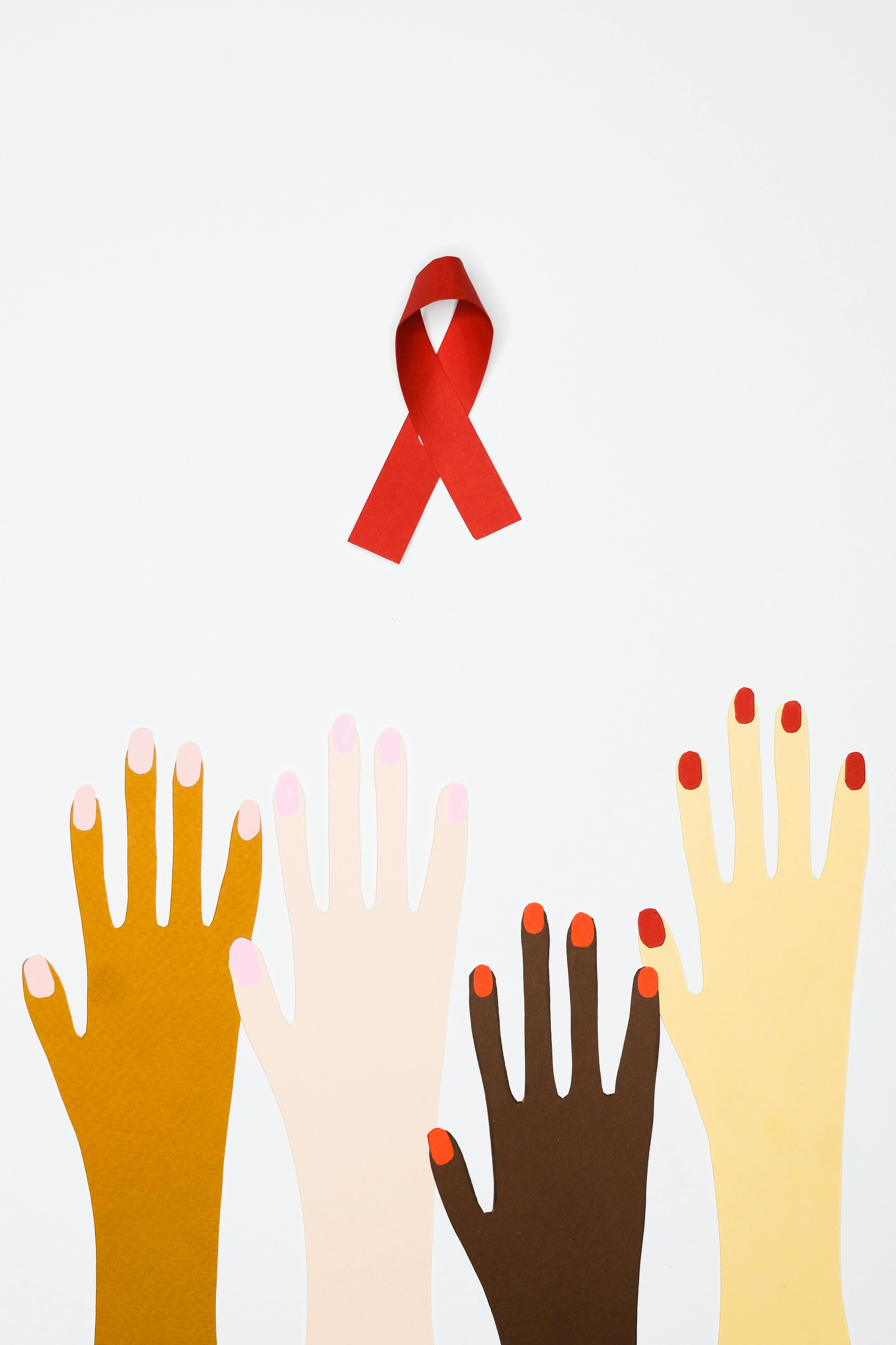 Conceptual image of diverse paper hands reaching towards a red awareness ribbon symbolizing support and unity.