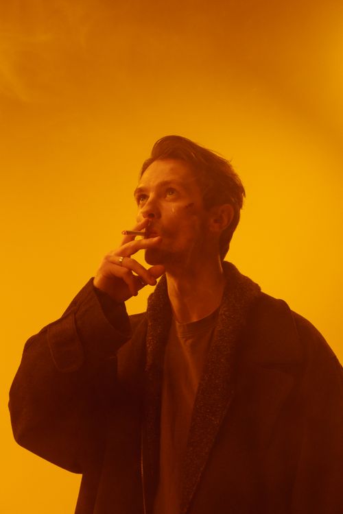 Free Moody portrait of a man smoking, enveloped in a dramatic orange haze, depicting addiction and contemplation. Stock Photo