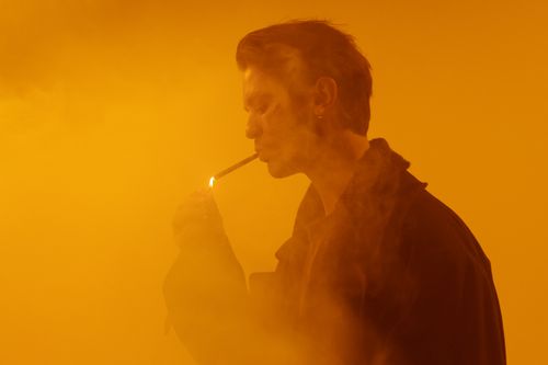 Free A man with short hair smoking in a hazy, amber-lit environment. Artistic and moody. Stock Photo
