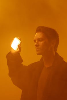 A contemplative man in a foggy, orange-tinted setting holds a glowing phone.