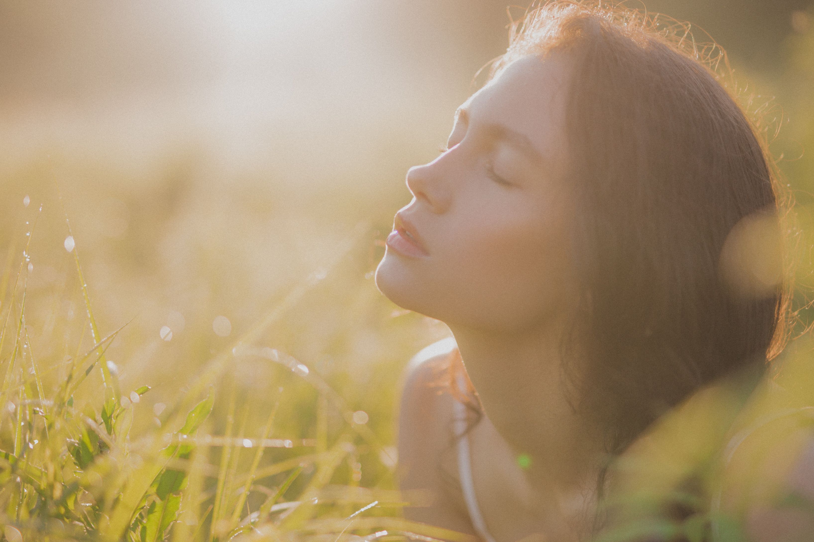 目を閉じた若い女性が草原の中で日光を楽しんでいます。