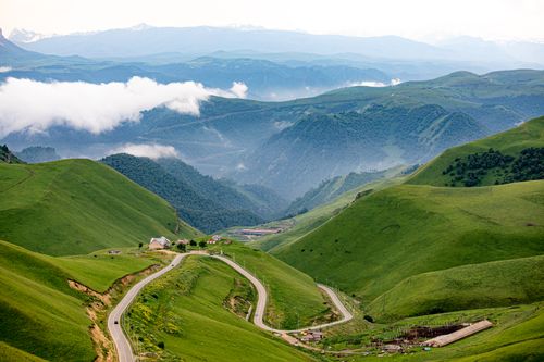 Free A breathtaking aerial view of a winding road through lush green hills in a mountainous region. Stock Photo