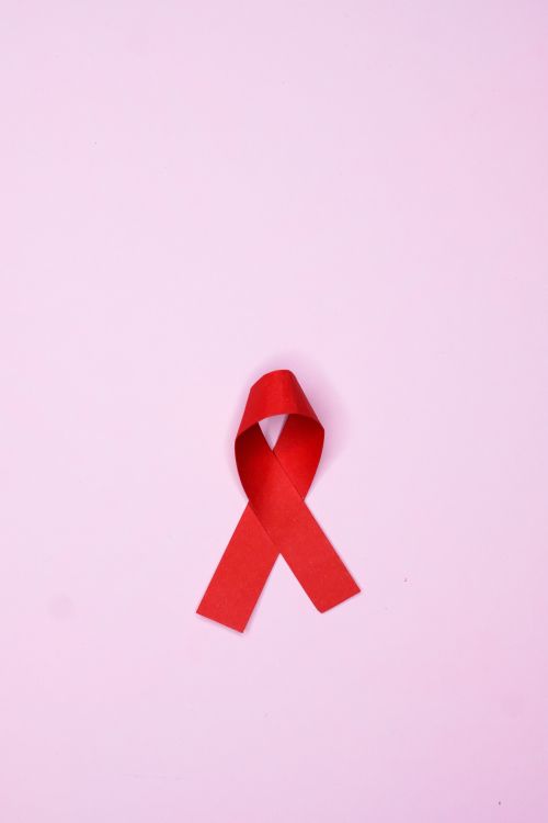 Free Vertical shot of a red ribbon symbolizing AIDS awareness on a pink background. Stock Photo