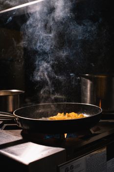 Frying pan with food and steam rising in a dark kitchen setting.
