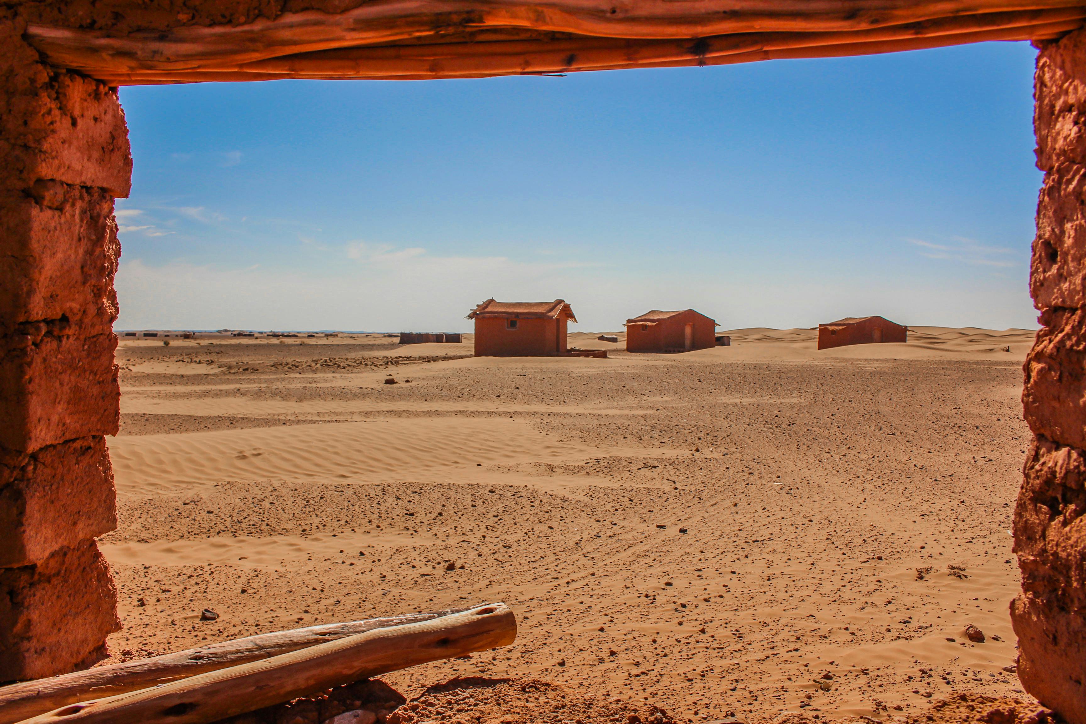 A scenic view of rustic huts in the vast Sahara Desert of Merzouga, Morocco, under a bright blue sky.