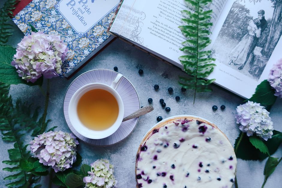 A cozy flat lay featuring tea, a blueberry cheesecake, and books for a relaxing vibe.