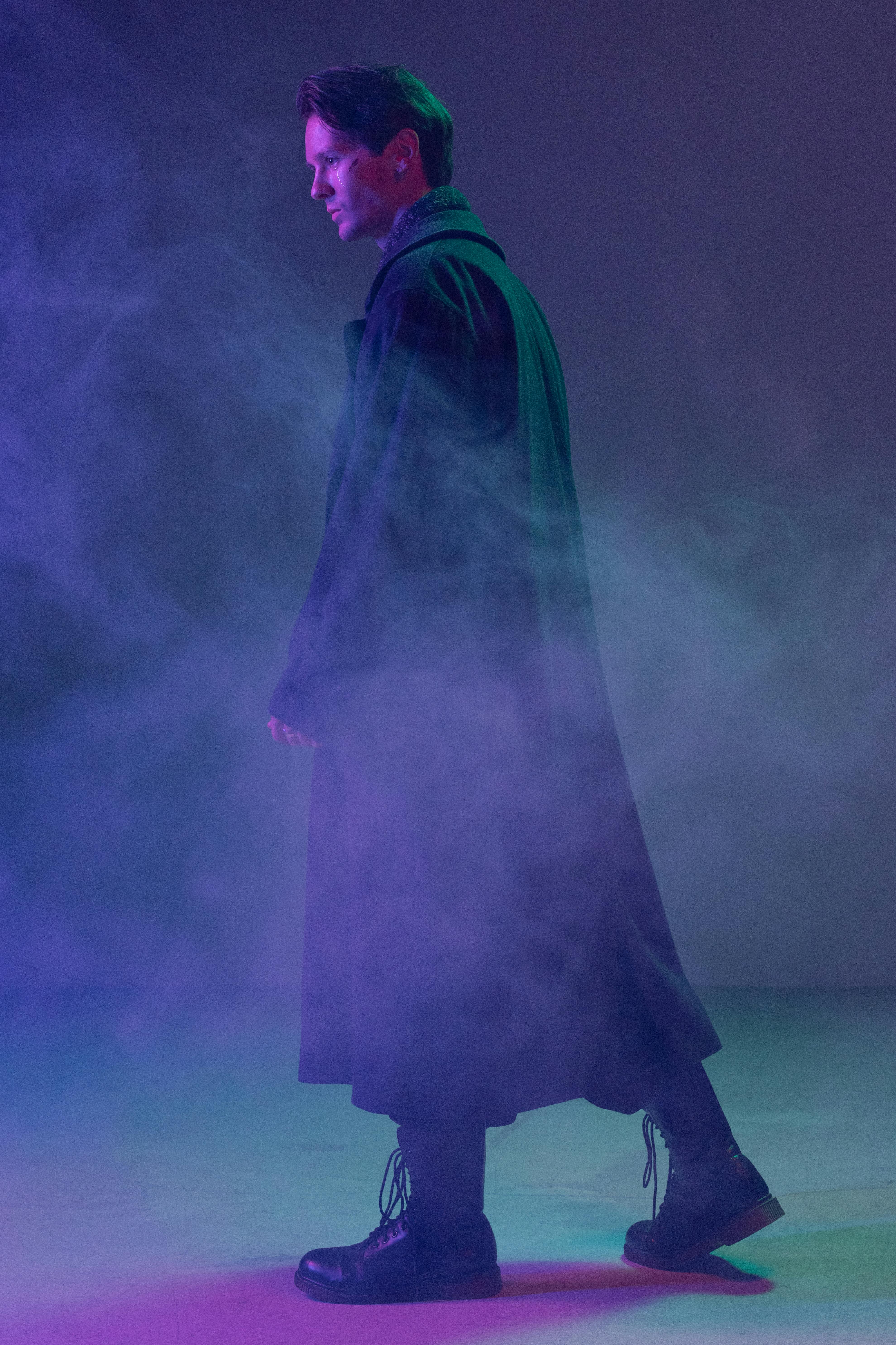 A man in a stylish coat walking through vibrant fog in a studio setting, exuding a cyberpunk vibe.