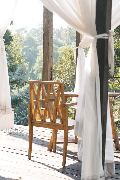 Free Relaxing outdoor patio with wooden chair and flowing curtains in a natural setting. Stock Photo