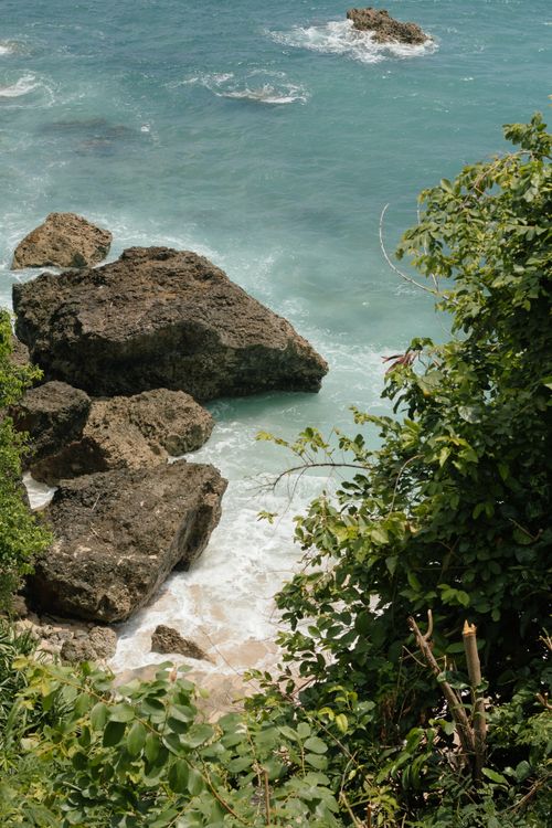 Free A stunning view of a rocky coastline with lush greenery and ocean waves crashing against the boulders. Stock Photo